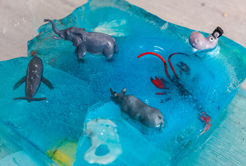 Expérimentation sensorielle : figurines d’animaux libérées d’un bloc de glace coloré – motricité fine et découverte.
