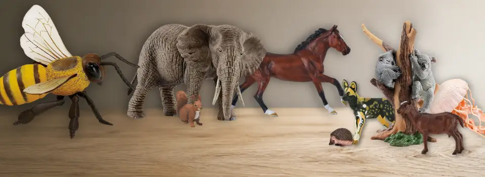 Figurines d'animaux réalistes alignées sur un plan de travail en bois clair : éléphant d'Afrique, cheval, écureuil roux, lycaon, hérisson et koalas sur un tronc